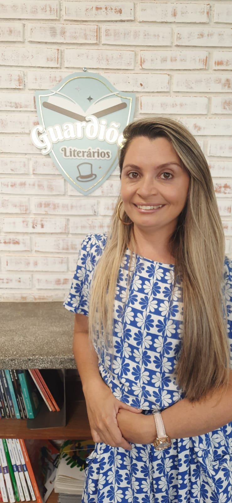 Gi Santos, idealizadora dos Guardiões Literários, sorrindo diante do escudo da marca